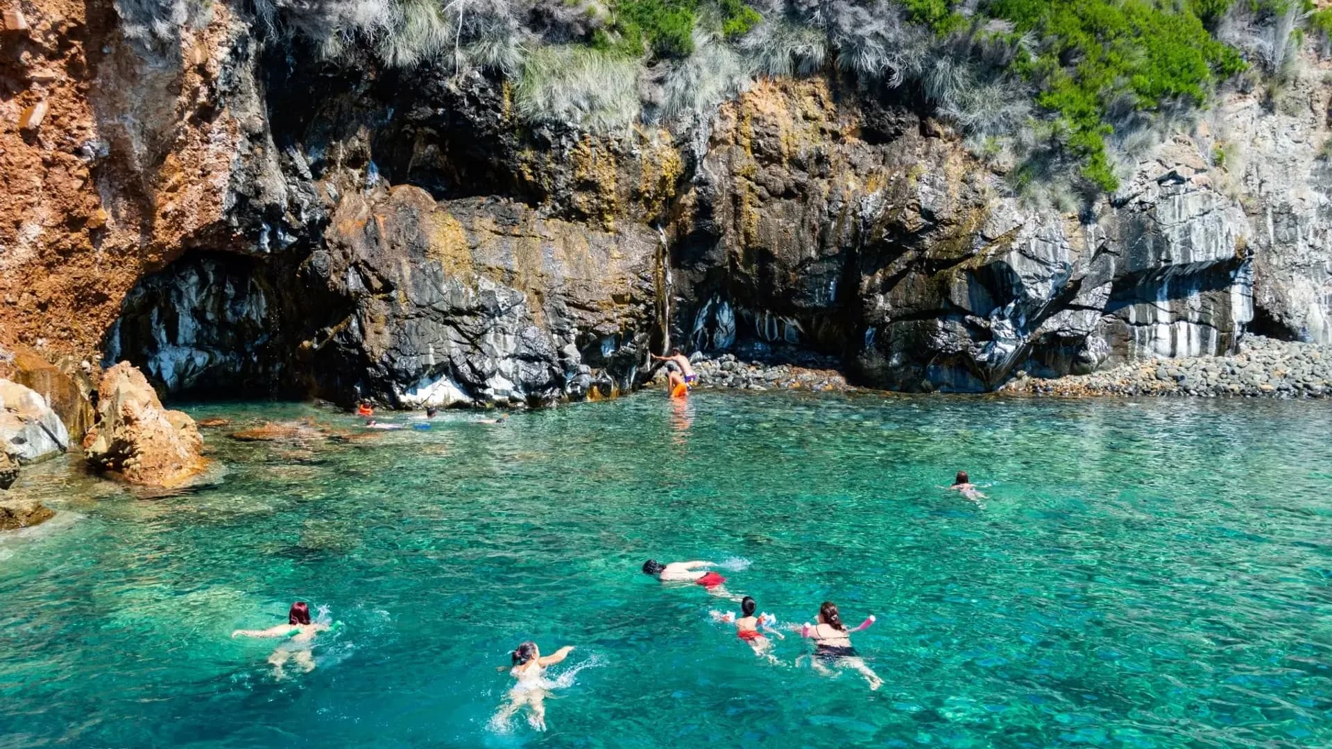 Swimmers beside a rocky coastal cave