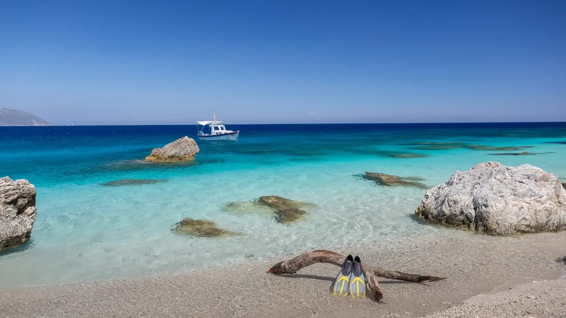 Clear shallow water beside a pale beach and rocks
