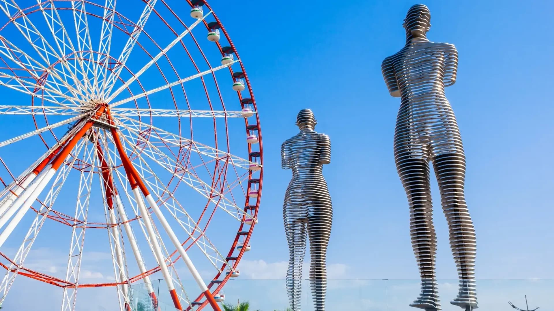 Metal figures beside a large Ferris wheel