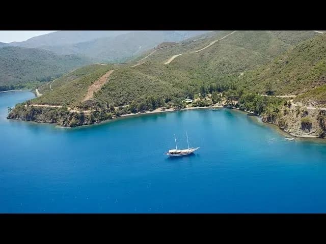 Yeşil tepelerle çevrili bir koyda yelkenli tekne