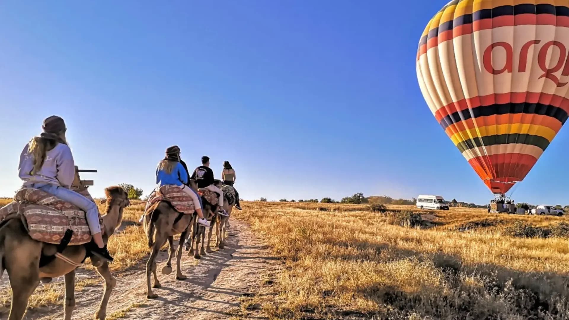 Camel riders with a balloon in the background