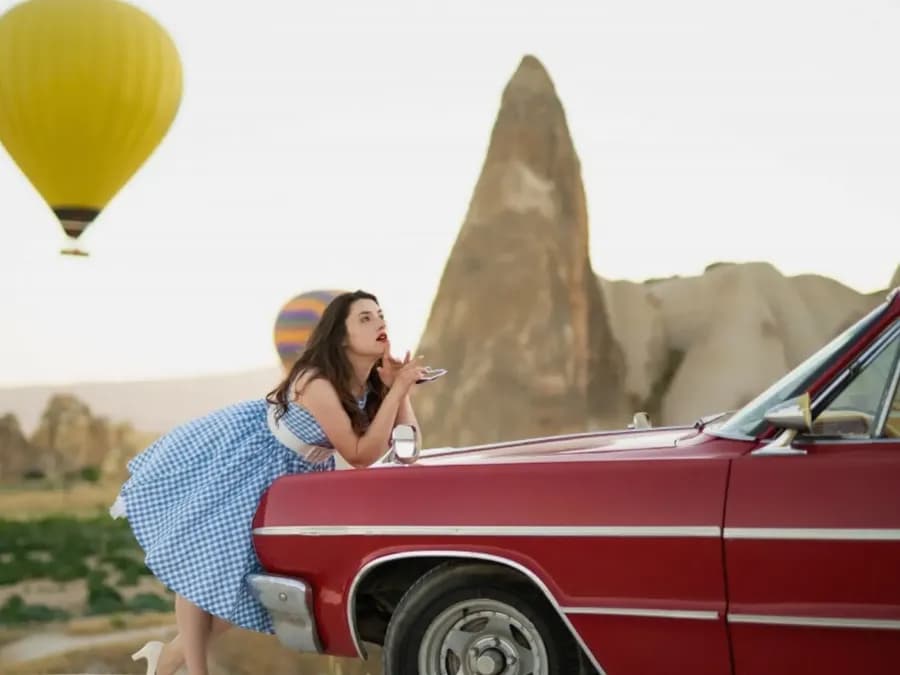Frau neben einem roten Oldtimer und Felsformationen