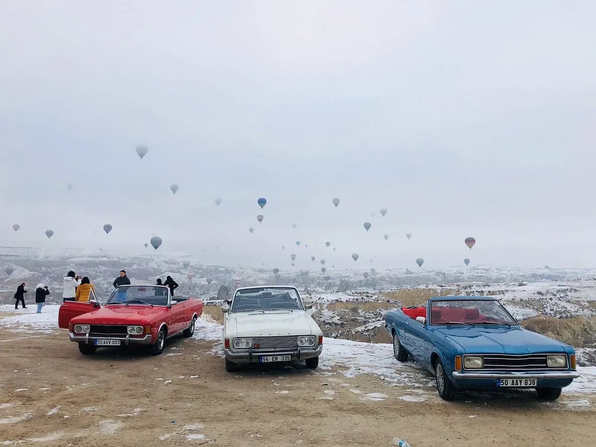 Uzakta sıcak hava balonlarıyla park edilmiş klasik arabalar