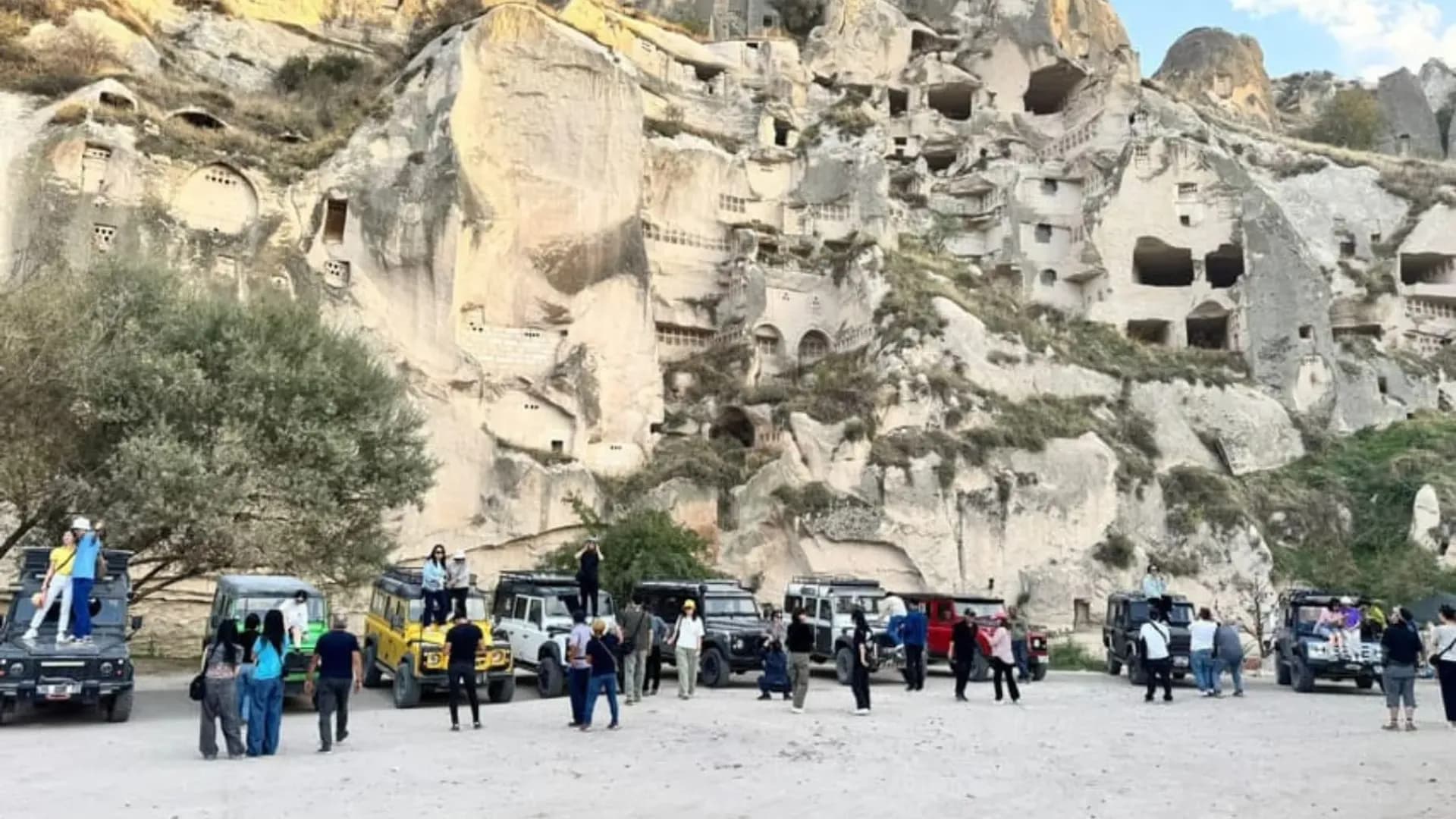 Visitors and vehicles beside a rocky cliff