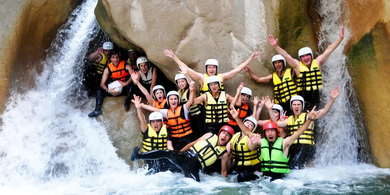 Gruppe mit Helmen und Schwimmwesten neben einem Wasserfall