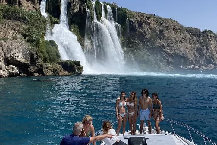 Bootsgäste unter einem Wasserfall, der ins Meer mündet